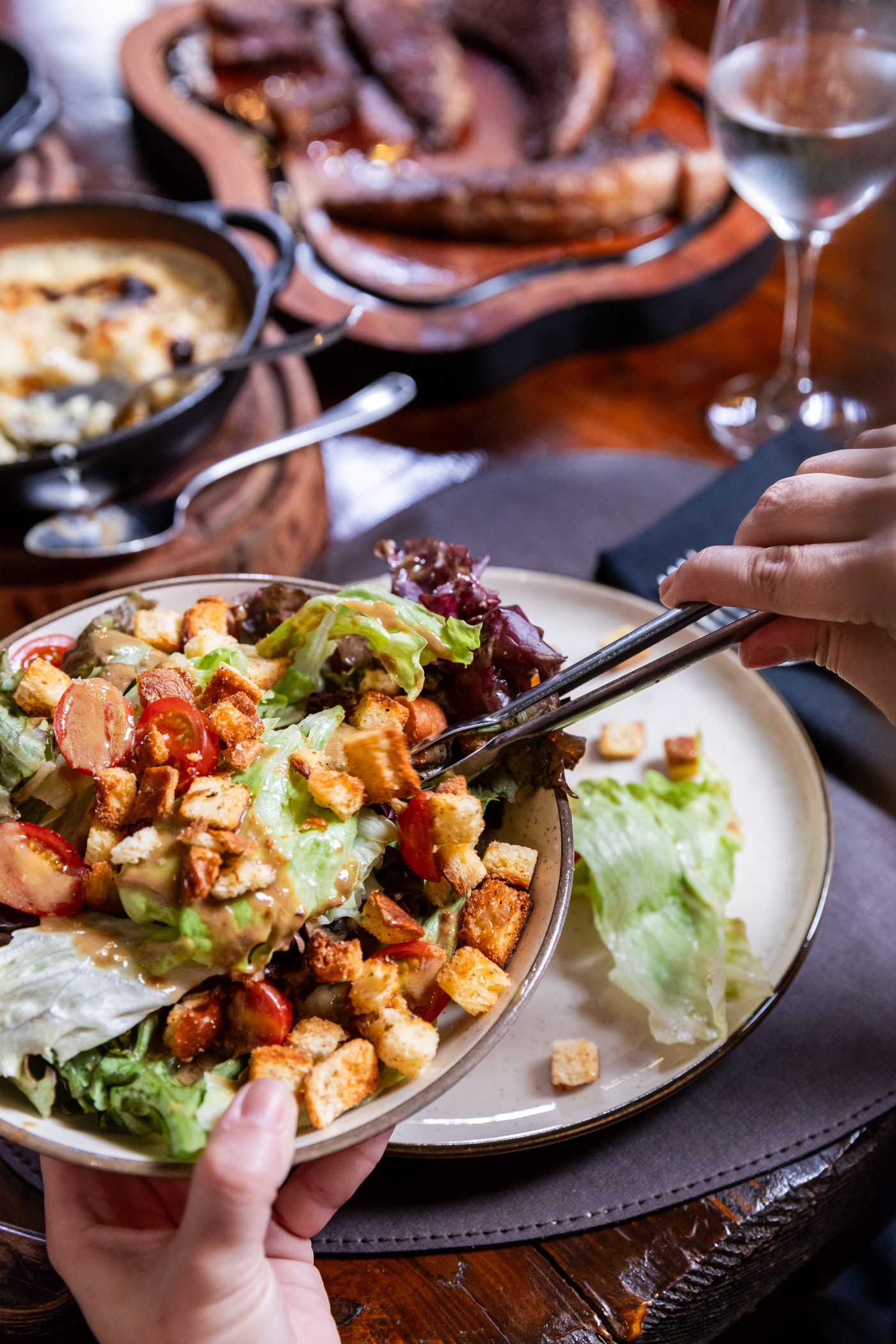 Mesa completa: salada da casa sendo servida, guarnições e tábua de cortes ao fundo